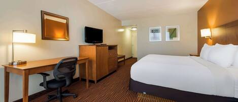 A hotel room with a bed, desk, chair, television, and wall-mounted lamps.