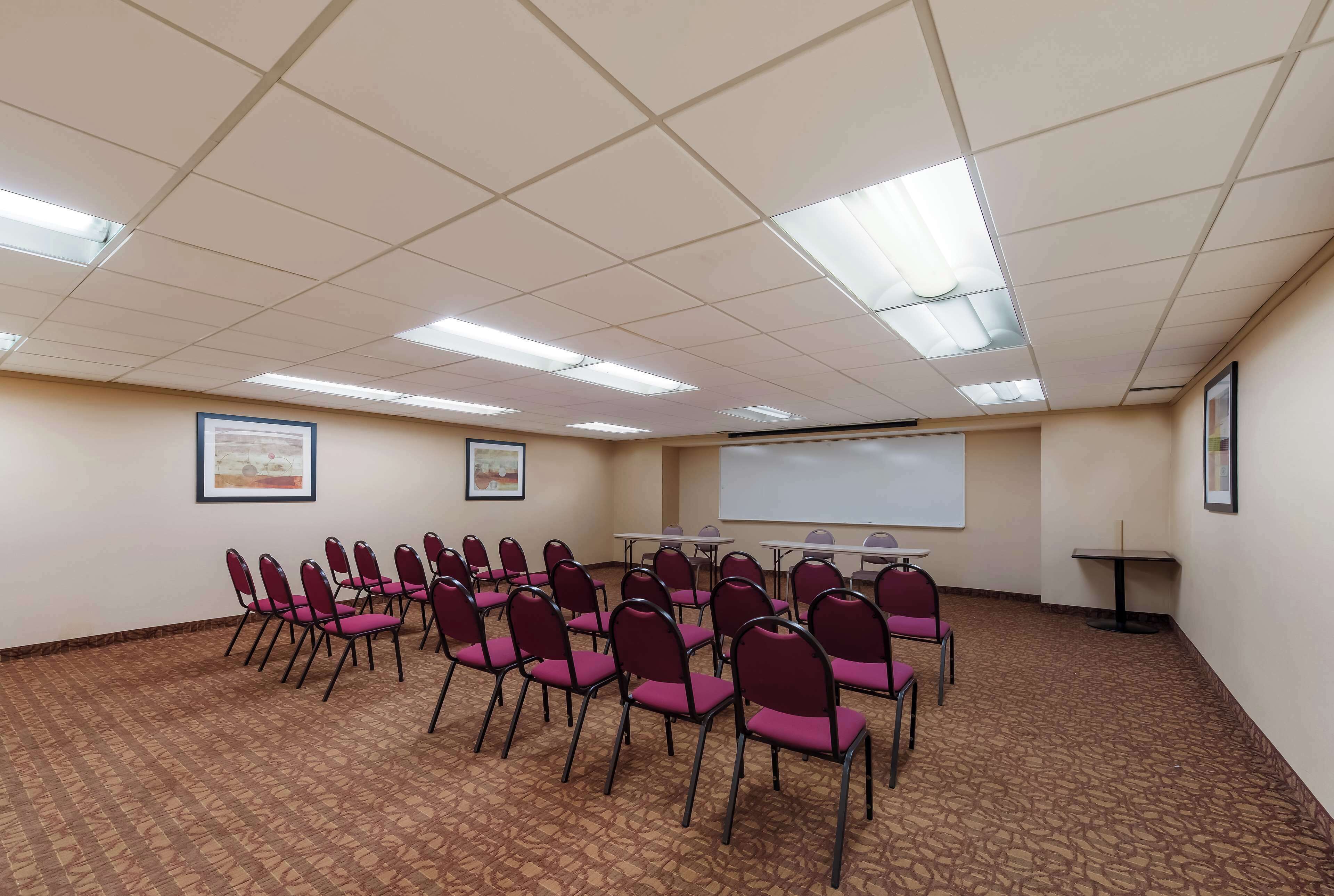 A conference room with rows of chairs, a projector screen, and framed pictures on the walls.