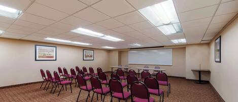 A conference room with rows of chairs, a projector screen, and framed pictures on the walls.