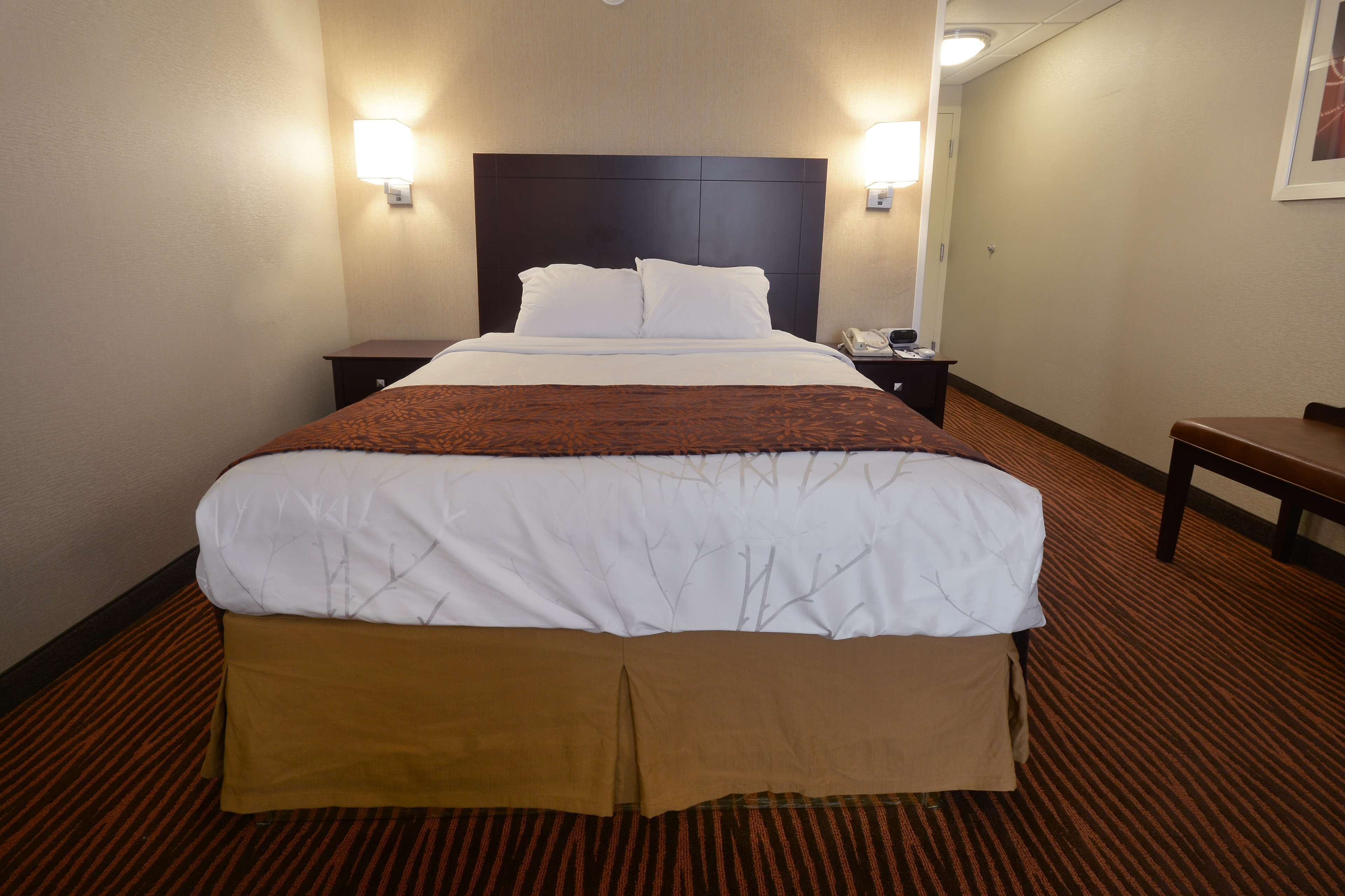 A hotel room with a large bed, two bedside tables, a nightstand, and a chair.