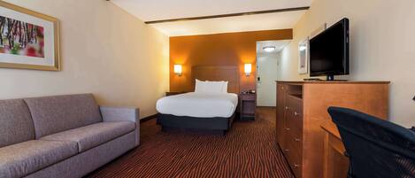 Una habitación de hotel con cama, sofá, televisor y escritorio.