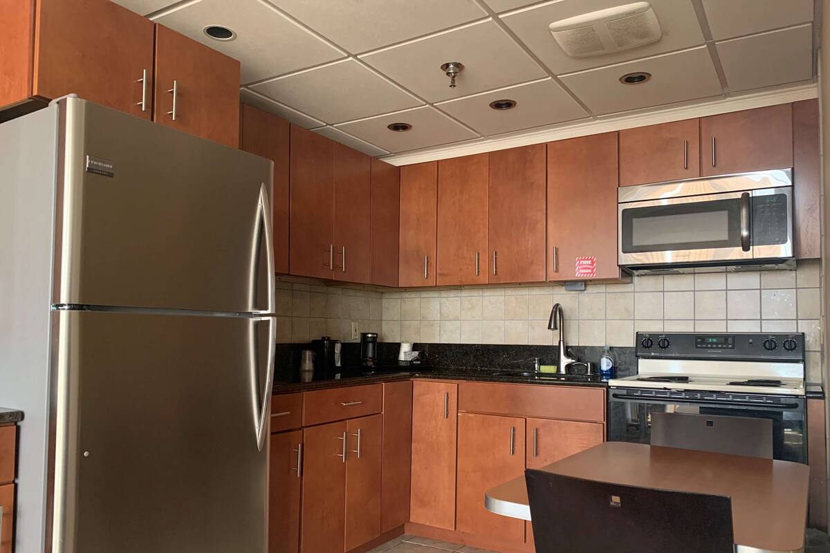 A kitchen with wooden cabinets, a stainless steel refrigerator, a microwave, a stove, and a sink.