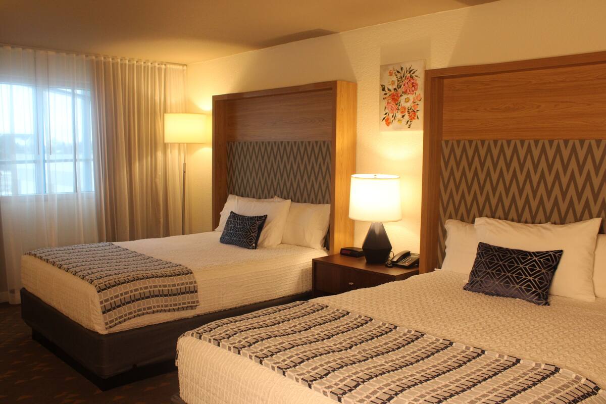 Two double beds with patterned bedding, bedside lamps, and a decorative wall piece.