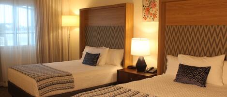 Two double beds with patterned bedding, bedside lamps, and a decorative wall piece.