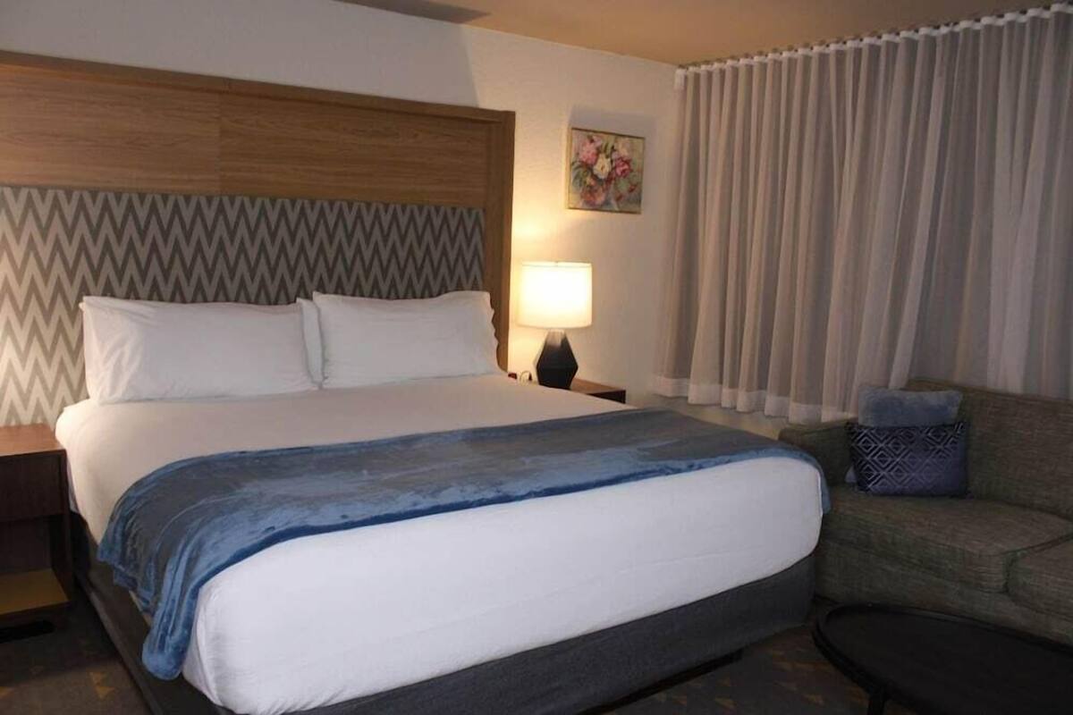 A hotel room with a bed, a nightstand, a lamp, a couch, and a painting on the wall.