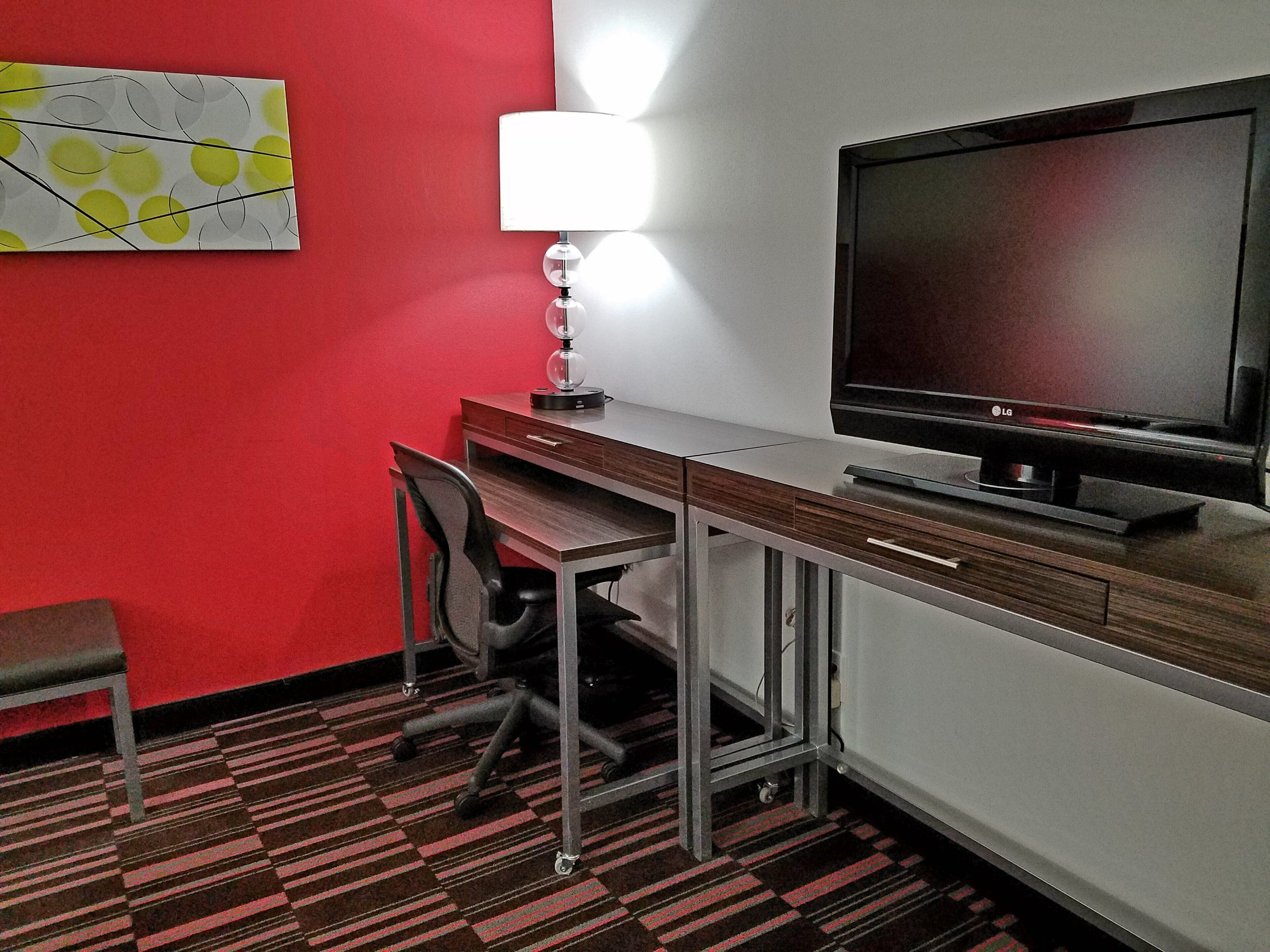 Una habitación de hotel con escritorio, silla, televisor y lámpara.
