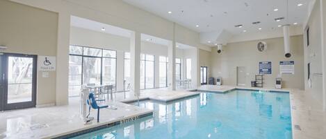An indoor swimming pool with clear glass walls, a pool lift, and a sign indicating a pool lift.