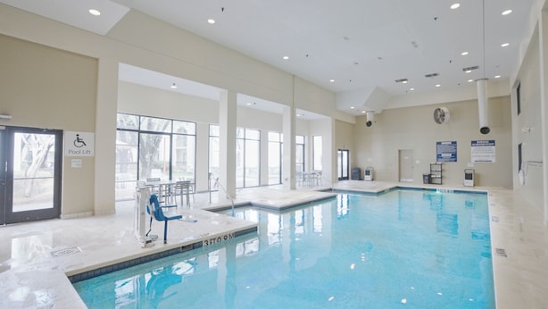 An indoor swimming pool with clear glass walls, a pool lift, and a sign indicating a pool lift.