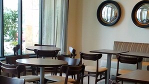 A dining area with multiple tables and chairs, large windows with curtains, and two wall-mounted mirrors.