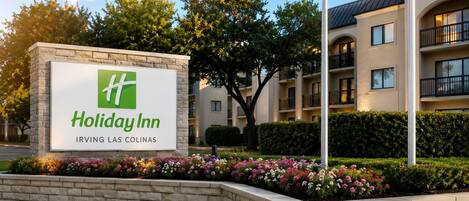 A Holiday Inn sign with a stone base and a landscaped flower bed in front.