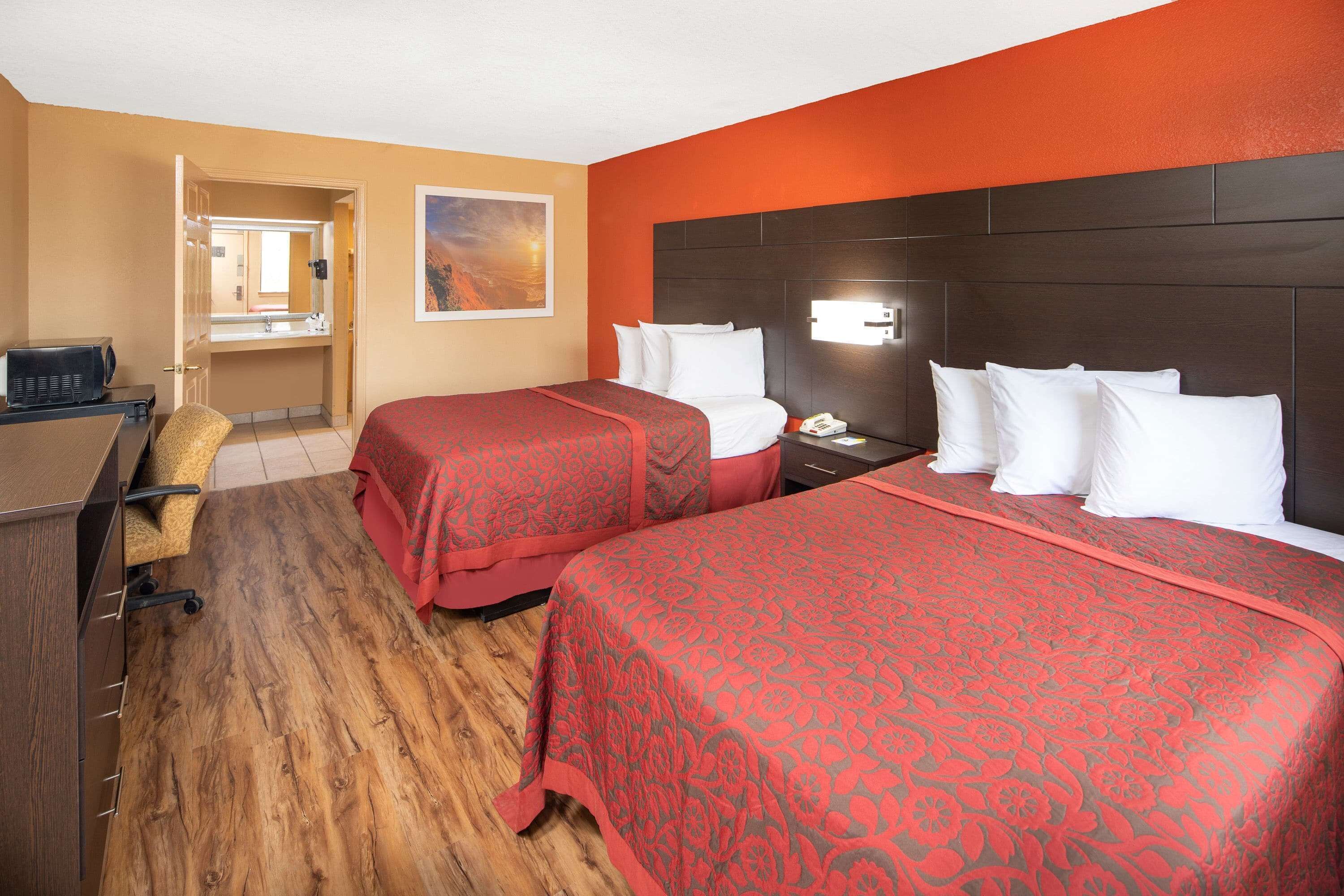 A hotel room with two beds, a desk, a chair, and a bathroom visible through an open door.