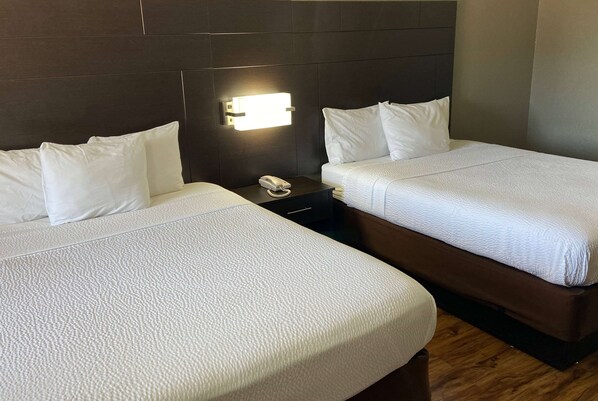 A hotel room with two beds, a nightstand with a phone, and a wall-mounted light. - Days Inn by Wyndham Tupelo (Tupelo)