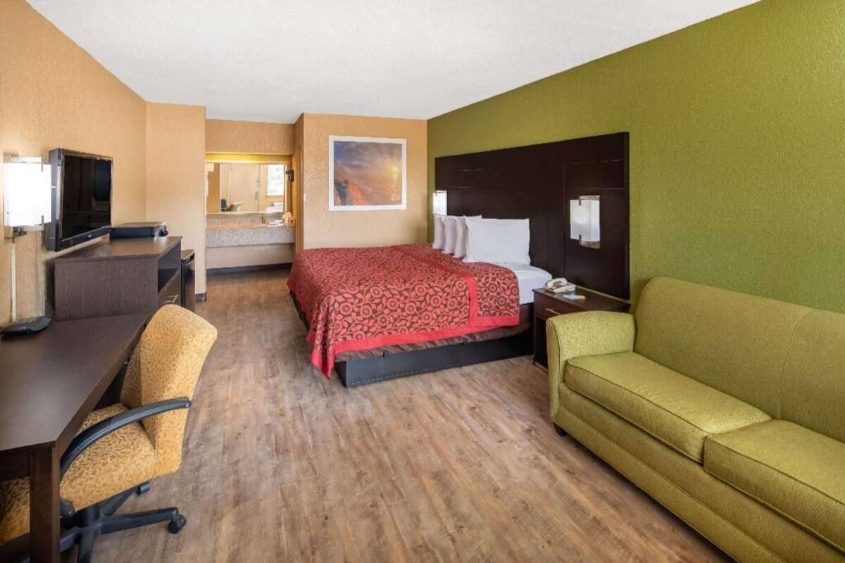Ett hotellrum med en säng, ett skrivbord med en stol, en soffa, en tv och en tavla på väggen.