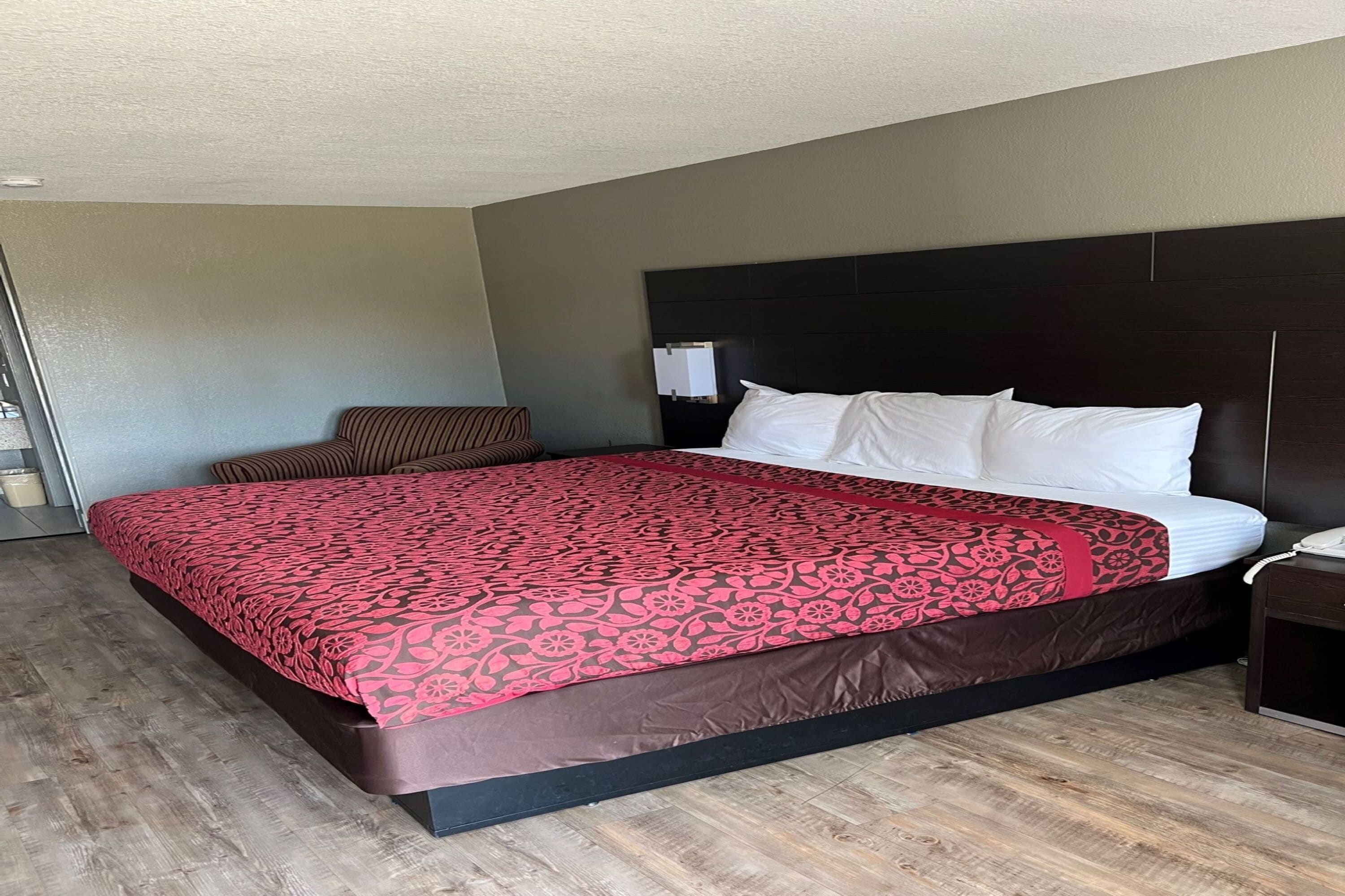 A hotel room with a large bed, a dark headboard, a bedside table with a lamp, and a wooden floor.