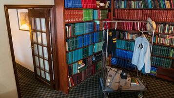 Ett bibliotek med bokhyllor fulla av böcker, en vagn med en jacka och en keps på, och en dörr som leder till ett annat rum.