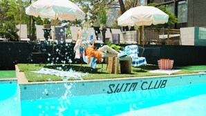 Zona de piscina con sombrillas, sillas de descanso y un cartel que dice "SWIM CLUB".