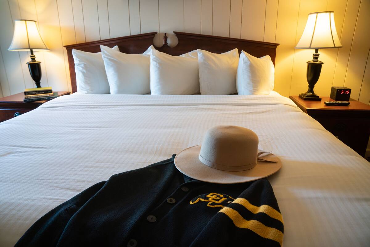A neatly made bed with white linens, a wooden headboard, and two bedside lamps.