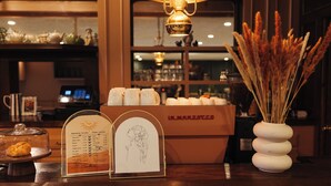 Una barra con una pizarra de menú, un jarrón decorativo con plantas secas y una vitrina con pasteles.