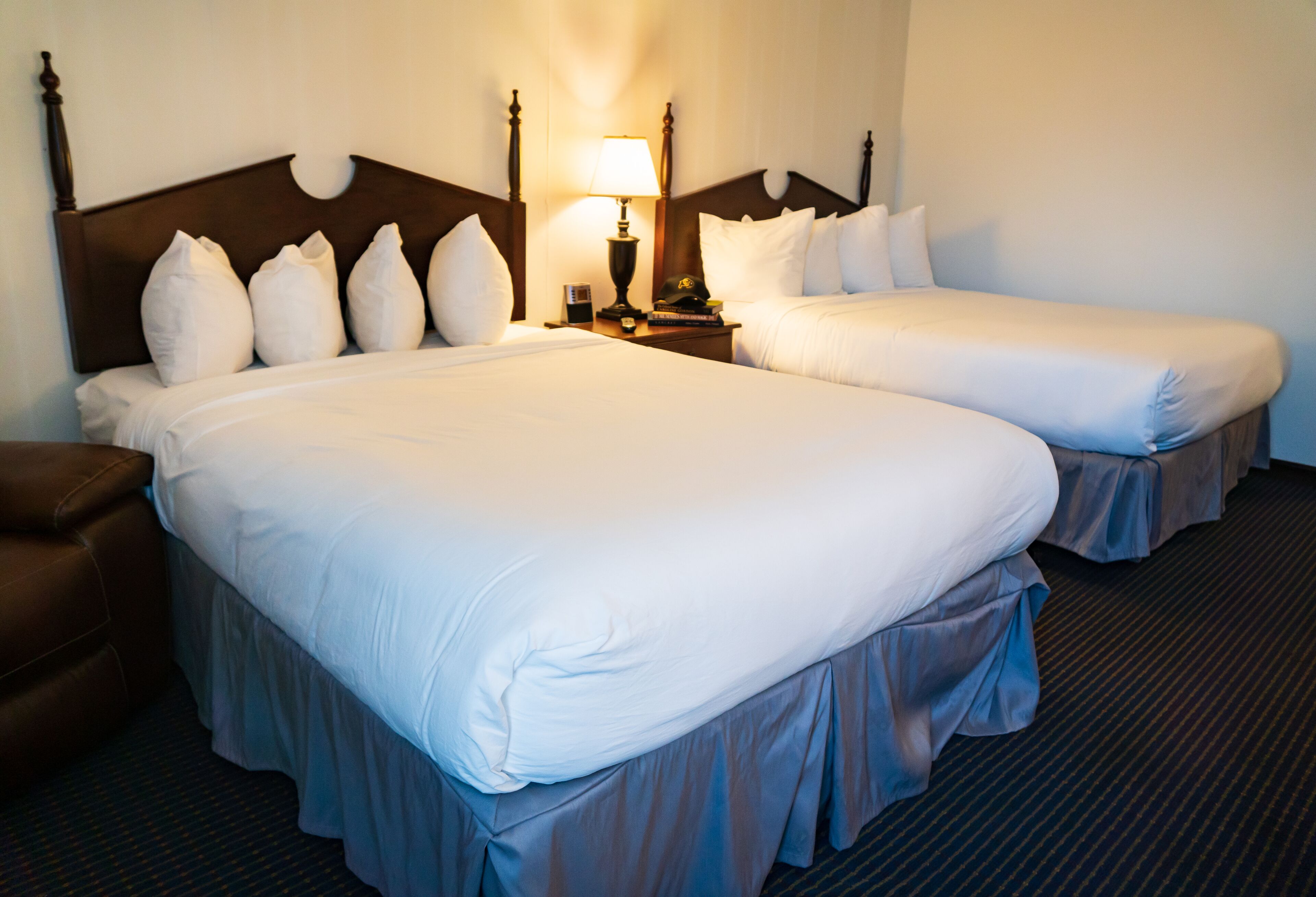 A hotel room with two beds, a nightstand with a lamp, and a brown leather chair.