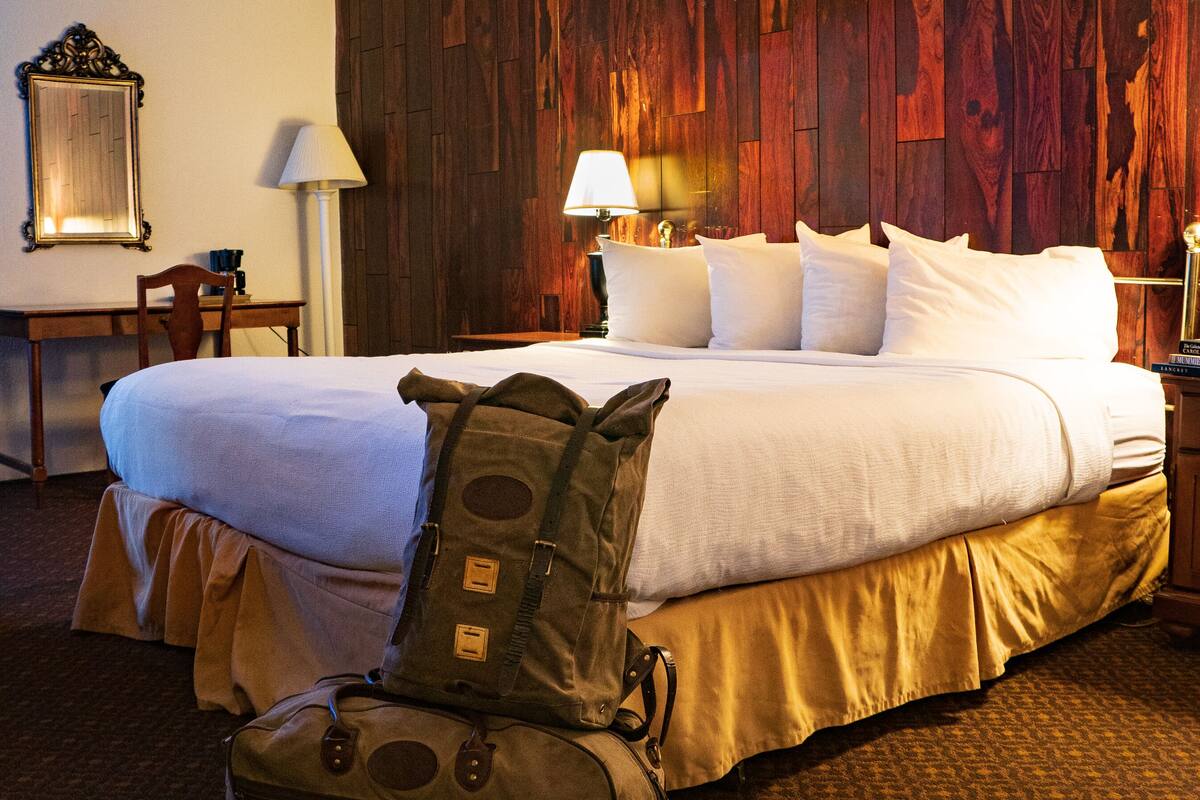 A hotel room with a large bed, a wooden headboard, a desk with a chair, and a lamp.