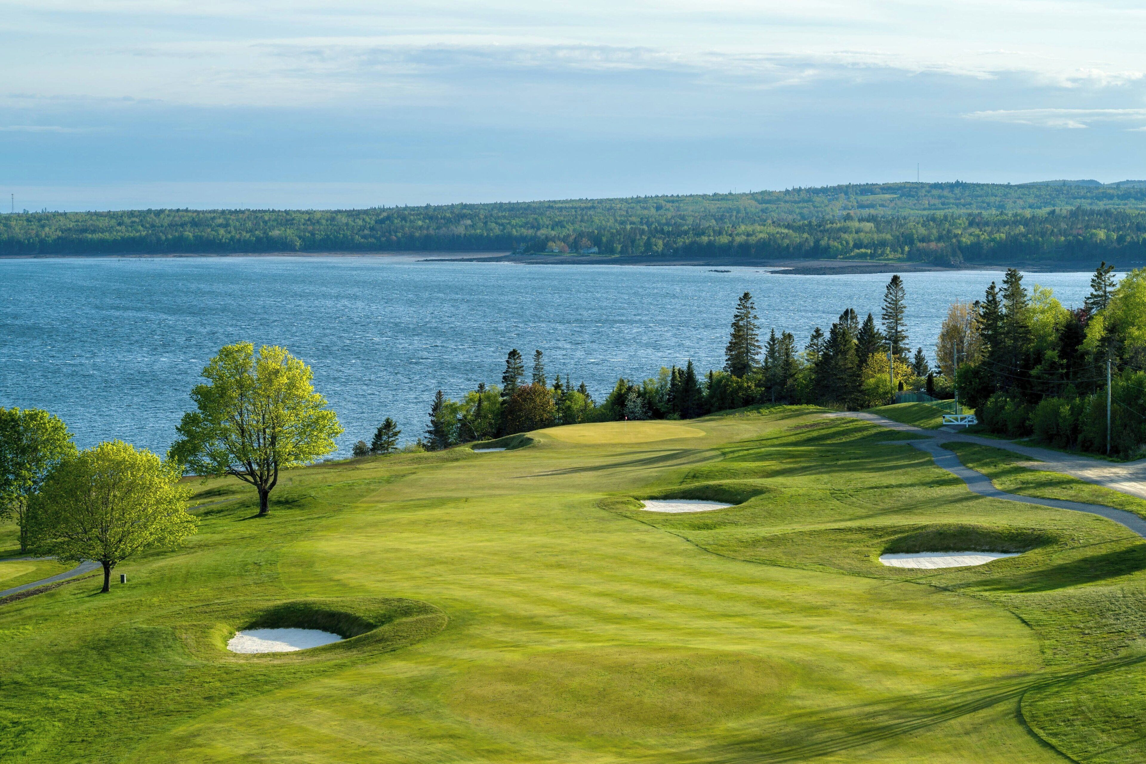 A golf course with bunkers, trees, and a body of water in the background.