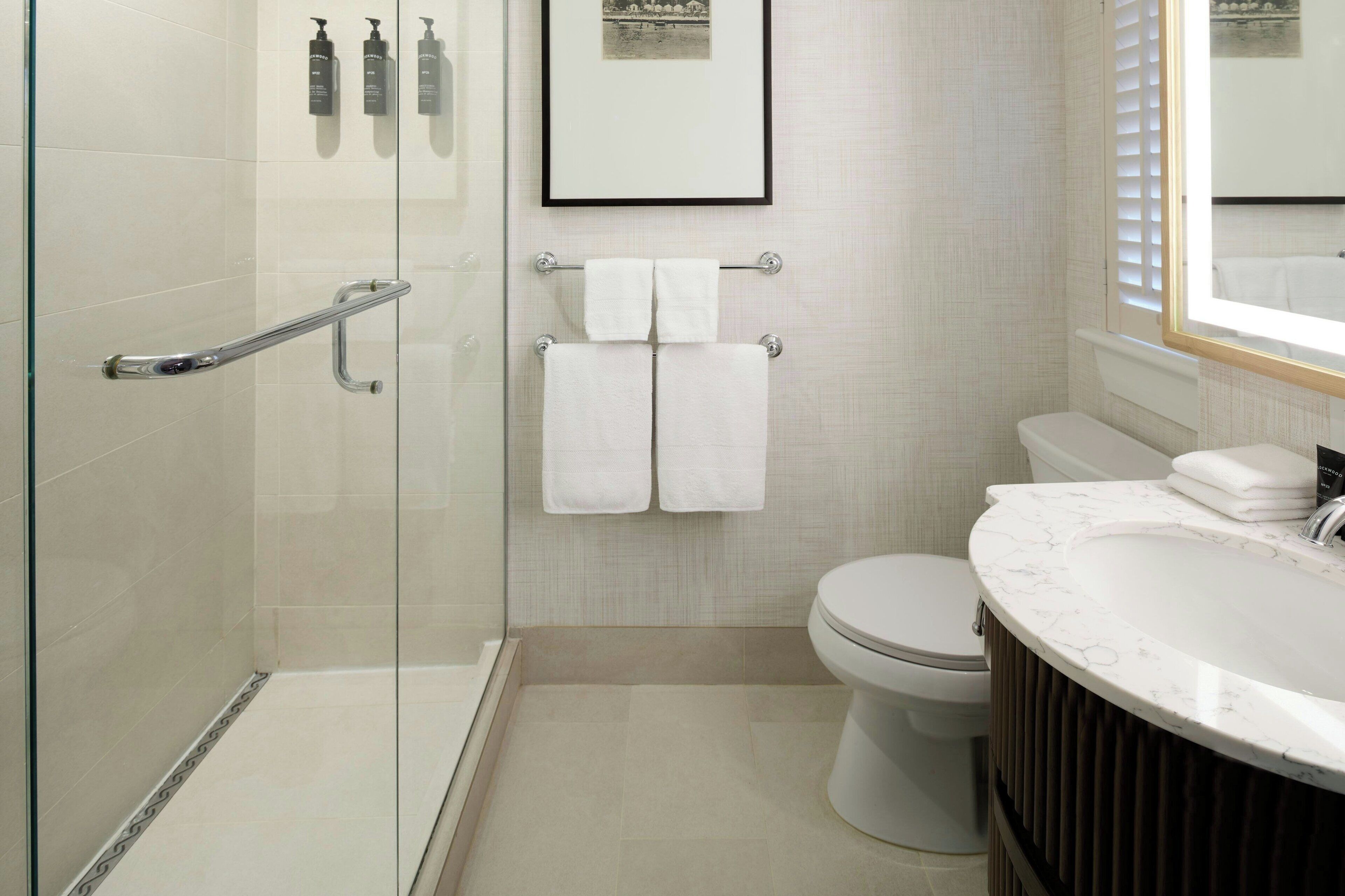 Un bany modern amb un espai de dutxa de vidre, un vàter i un lavabo amb taulell de marbre.
