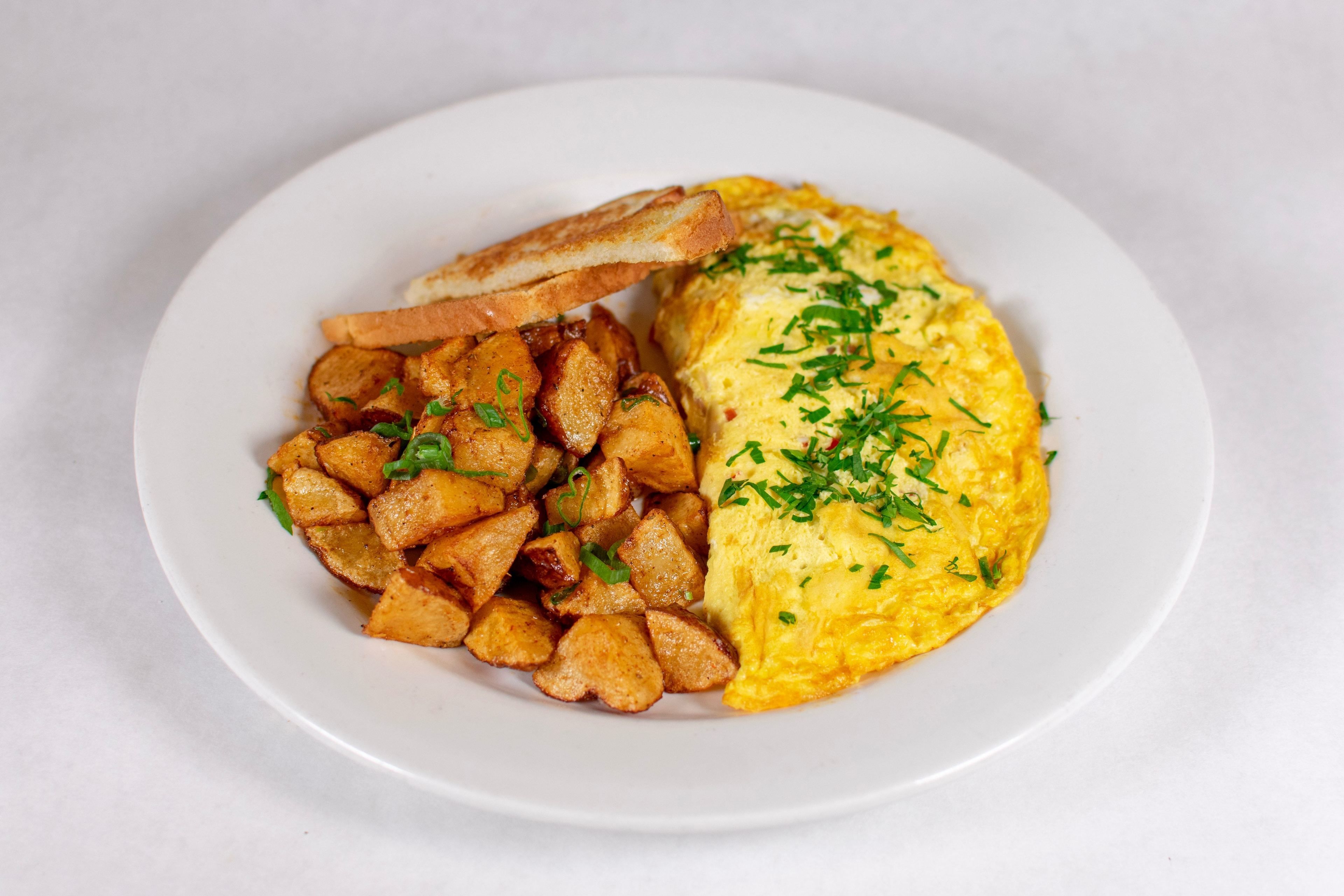 A plate with an omelette, fried potatoes, and a slice of toast.