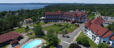 A large hotel with a swimming pool, surrounded by lush greenery and a view of a lake.