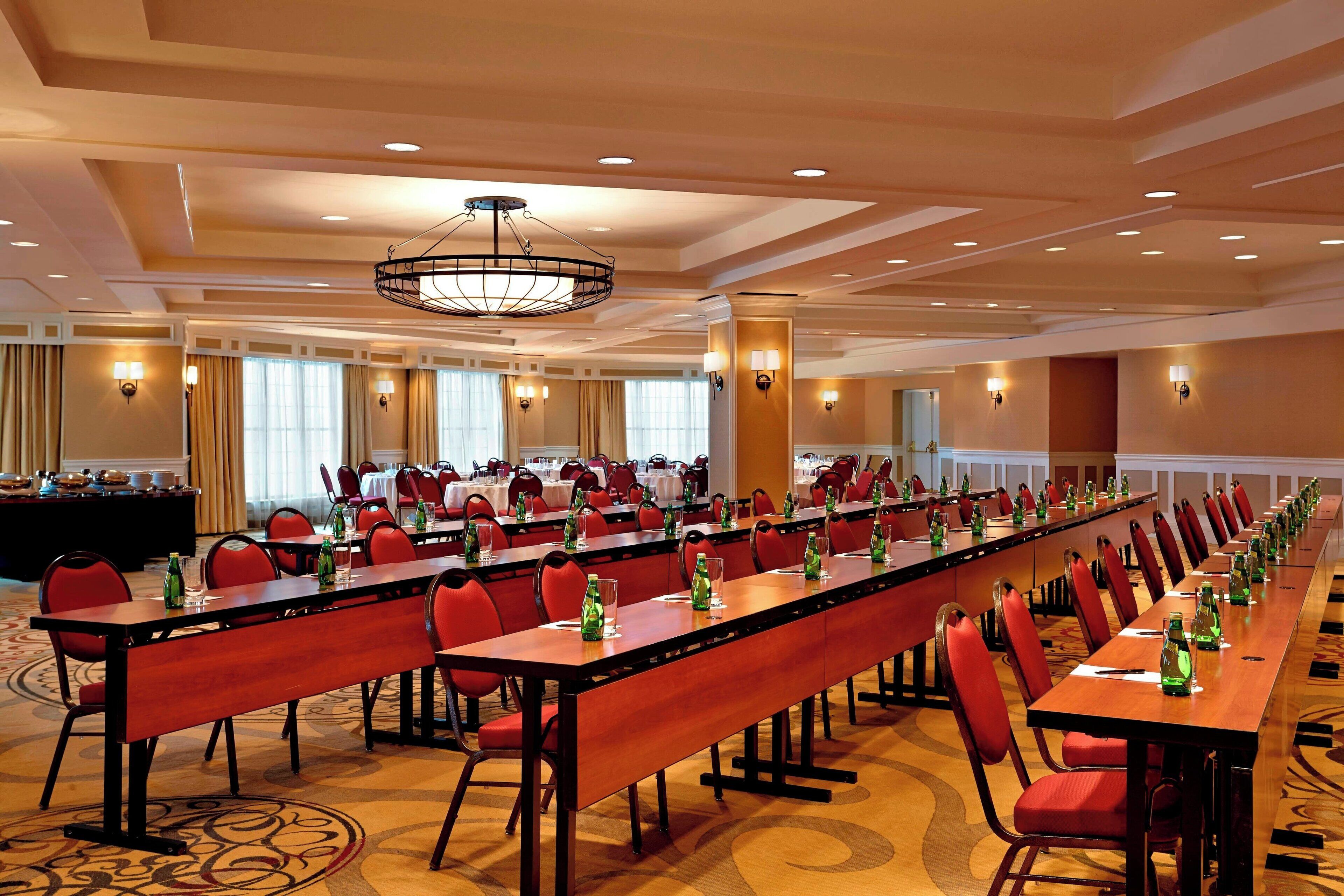 A conference room with long tables, red chairs, and a chandelier.