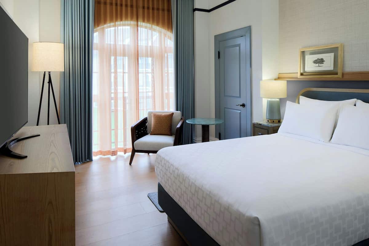 Une chambre d’hôtel avec un lit, un bureau, une chaise, une petite table et une porte.