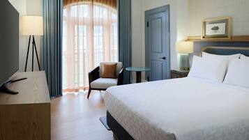 Habitación de hotel con cama, escritorio, silla, mesita y puerta.