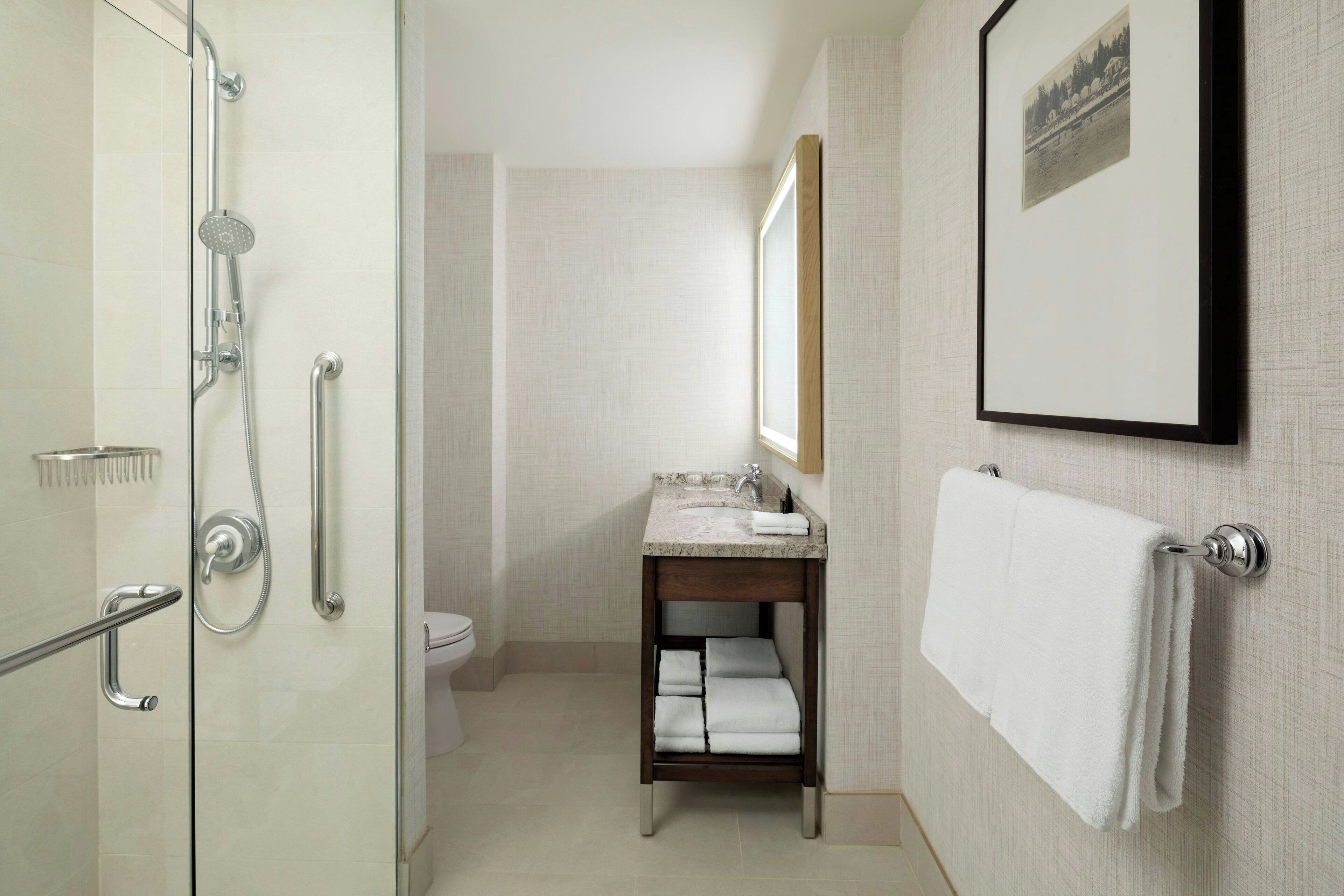 Un baño moderno con ducha envuelta en vidrio, lavamanos con espejo y un perchero para toallas.