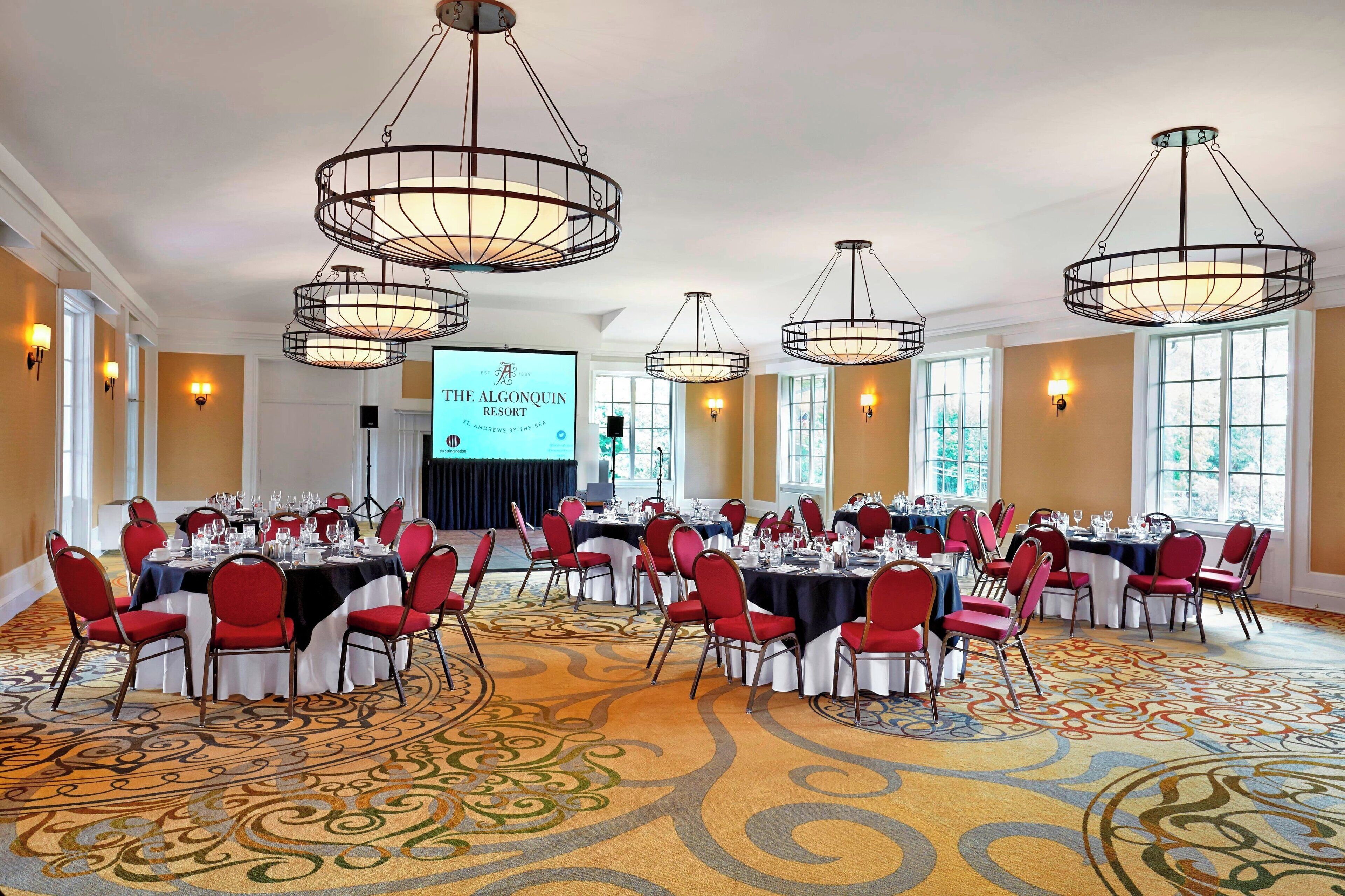 A conference room with round tables, red chairs, and chandeliers.