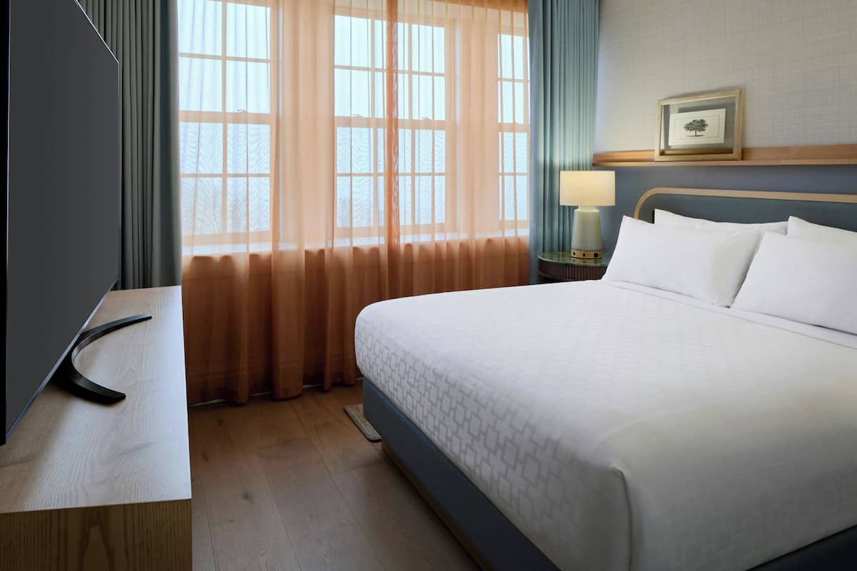 Une chambre d’hôtel avec un lit, un bureau, une lampe et une fenêtre avec des rideaux.