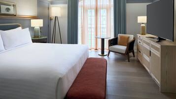 Ein Hotelzimmer mit einem großen Bett, einem Sessel, einem kleinen Tisch, einem Fernseher und einem Fenster mit Vorhängen.