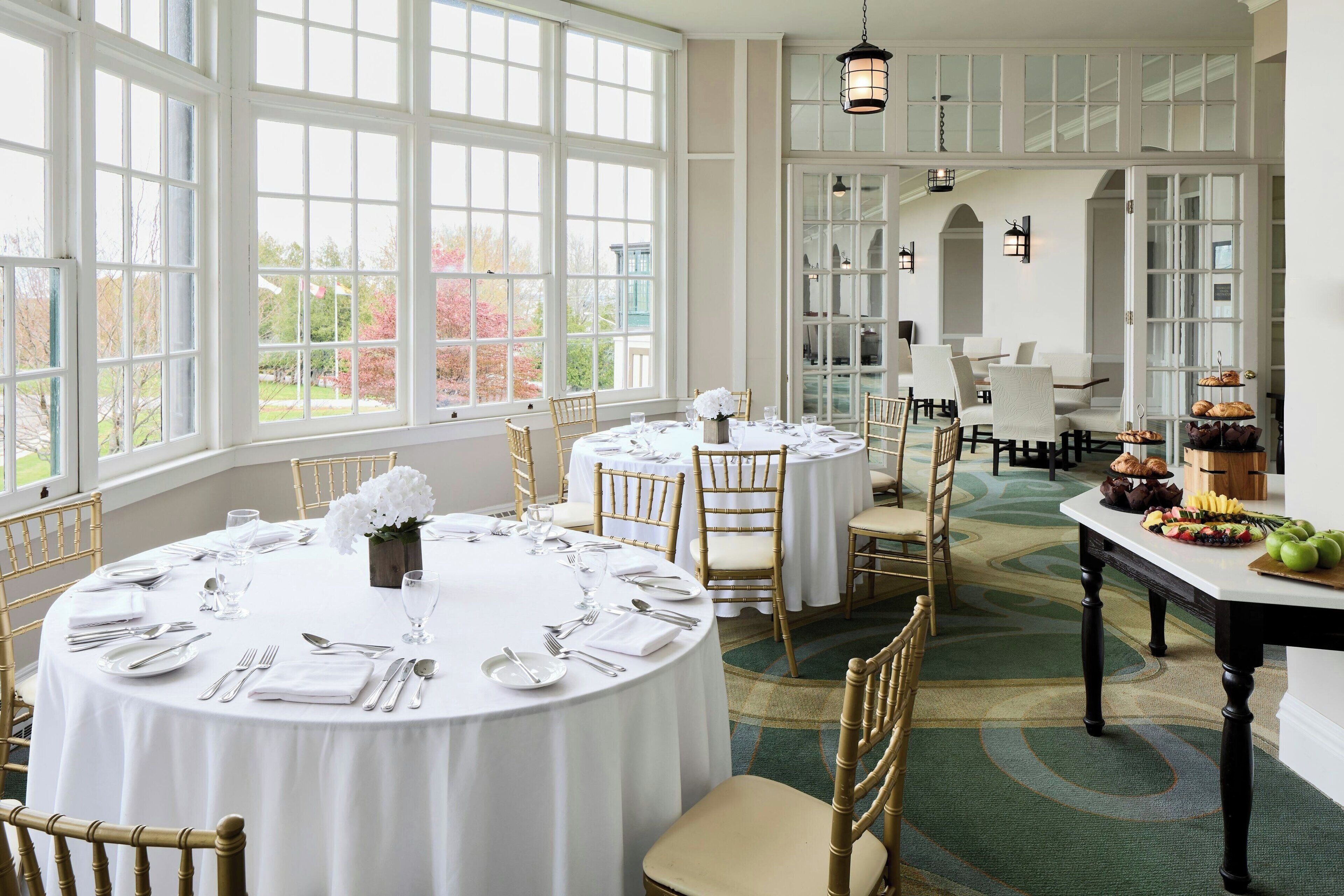 A dining area with round tables set for a meal, large windows, and a view of the outdoors.
