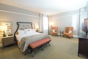 A hotel room with a large bed, a bench, two armchairs, a small table, a TV, and a nightstand with a lamp. - Algonquin Resort St Andrews by-the-Sea Autograph Collection (St. Andrews)