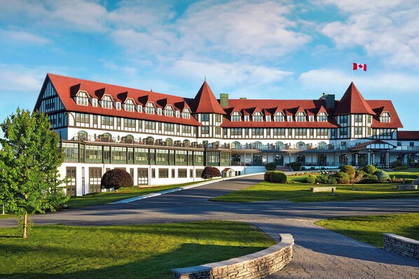 A large, modern hotel with a symmetrical facade, multiple red roofs, and a prominent Canadian flag. - Algonquin Resort St Andrews by-the-Sea Autograph Collection (St. Andrews)