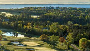 Campo de golf con búnkeres, un estanque y vistas a un lago y edificios a lo lejos.