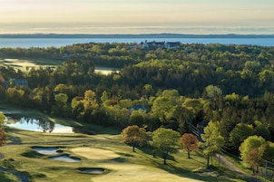 A golf course with bunkers, a pond, and a view of a lake and buildings in the distance.