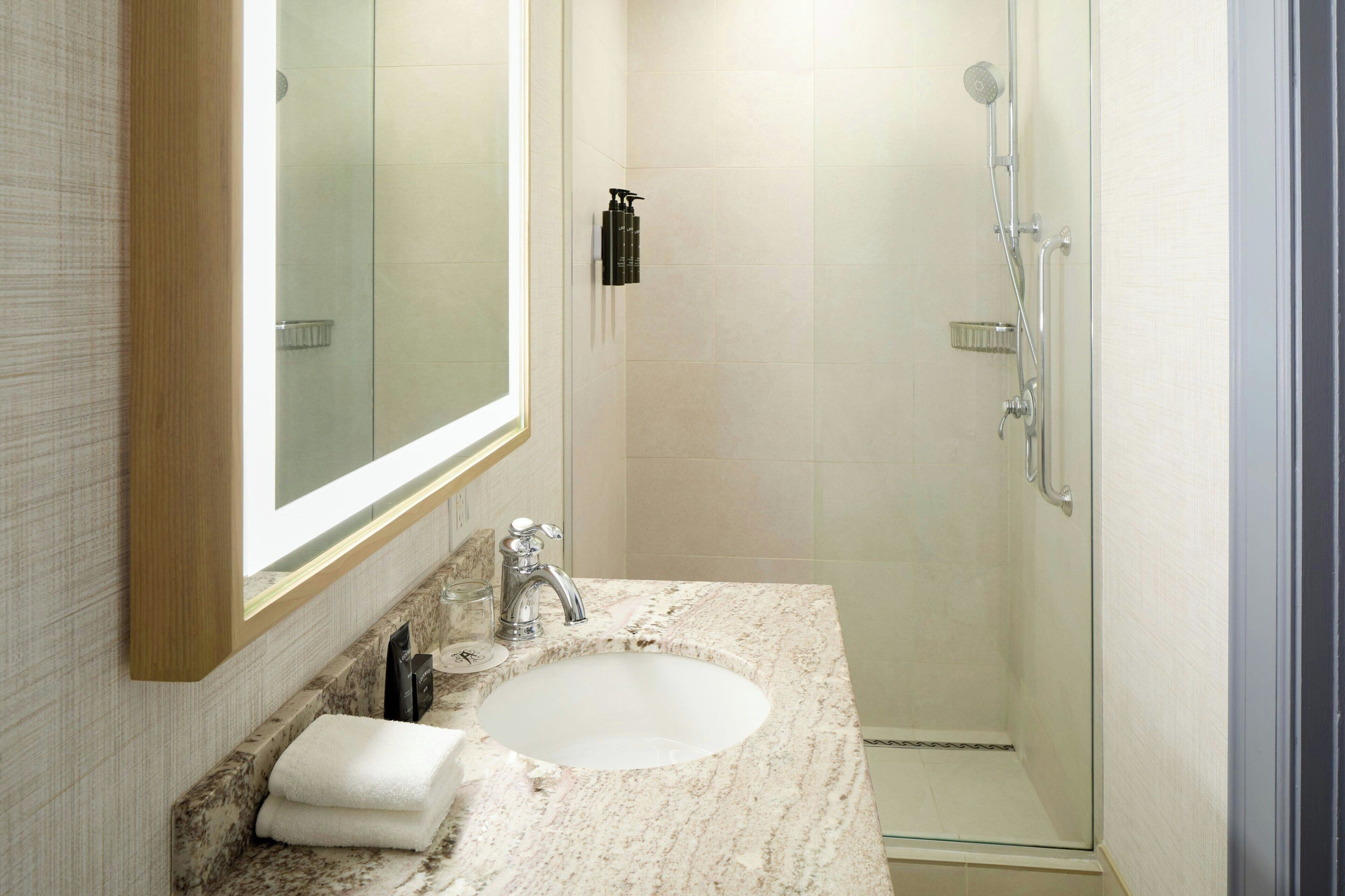 Un baño con lavamanos de mármol, un espejo grande y una ducha con cerramiento de vidrio.
