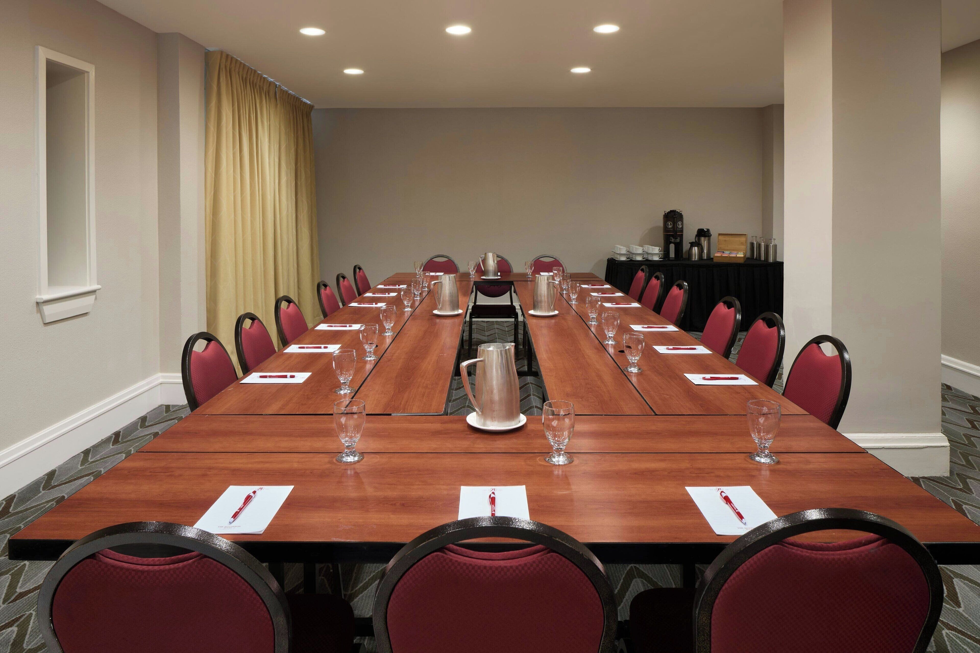 A conference room with a long table, red chairs, and a coffee pot.