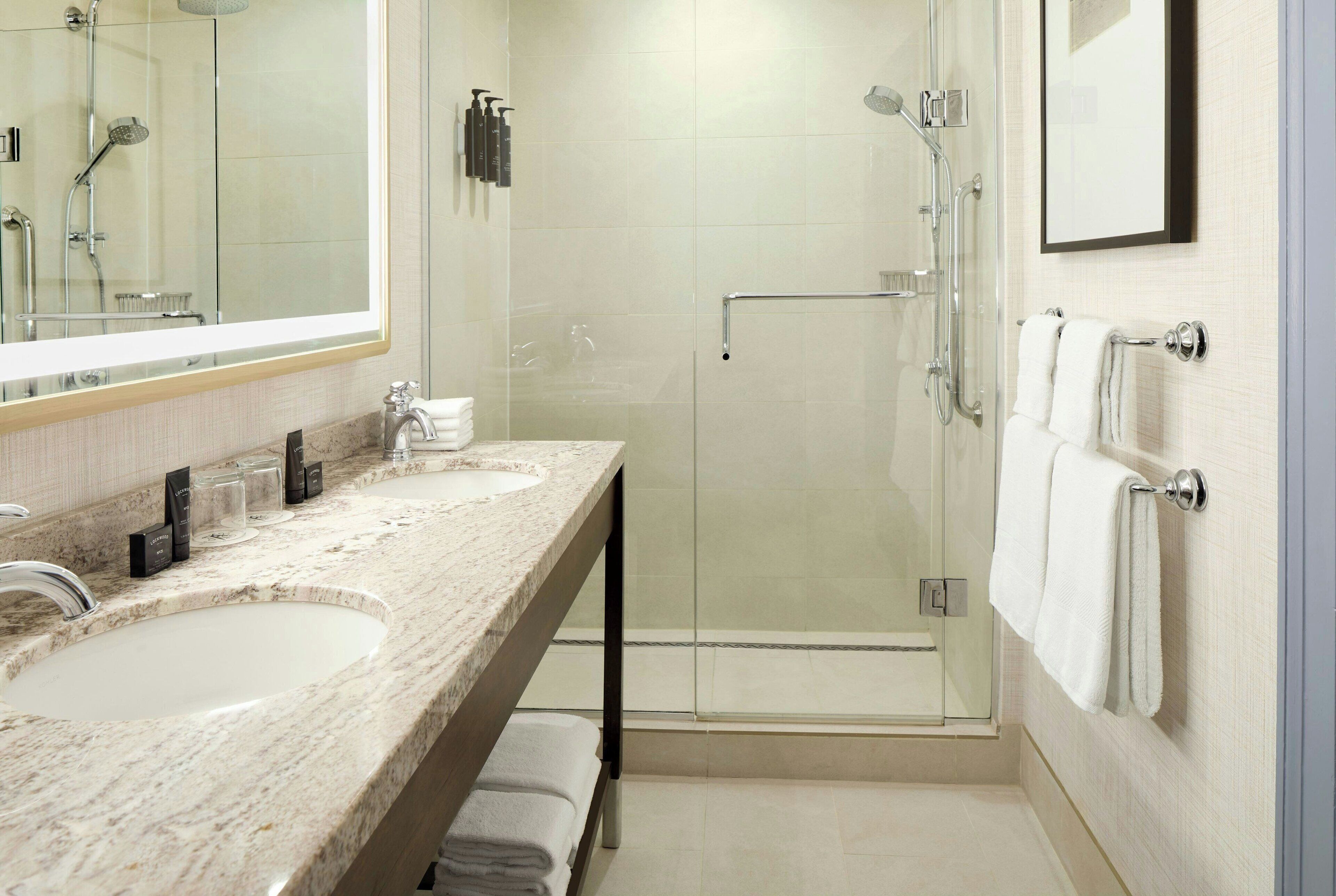 A modern bathroom with two sinks, a glass shower enclosure, and a large mirror.