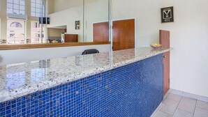 A reception area with a marble counter, blue mosaic tiles, a wooden door, and a framed certificate on the wall.