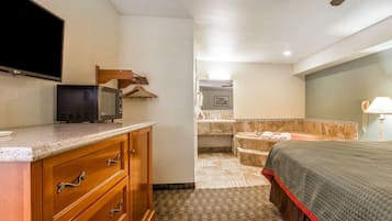 Habitación de hotel con televisor de pantalla plana, cómoda de madera, cama y baño con bañera y lavamanos.