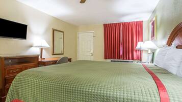 A hotel room with a bed, a desk, a chair, a television, a ceiling fan, and a window with red curtains.
