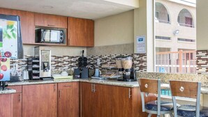 A kitchen area with wooden cabinets, a microwave, a coffee machine, and a breakfast bar with two bar stools.