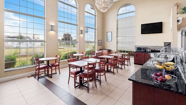 A spacious dining area with large windows, a chandelier, and a buffet counter with fruits and vegetables.