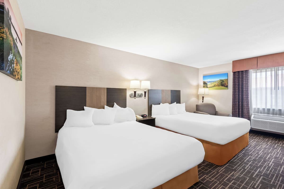 A hotel room with two beds, a nightstand, a lamp, and a painting on the wall.