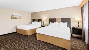 A hotel room with two beds, a nightstand with a lamp, a picture on the wall, and a patterned carpet.